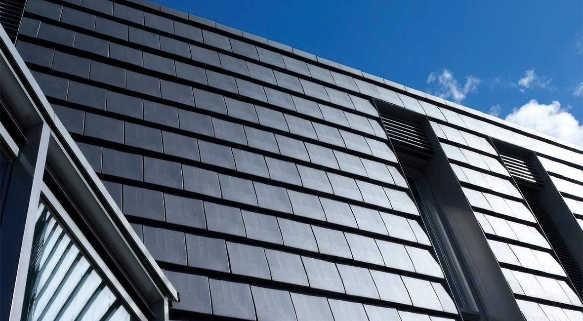 Schräges Dach mit dunklen Ziegeln, darüber klarer blauer Himmel (Foto)